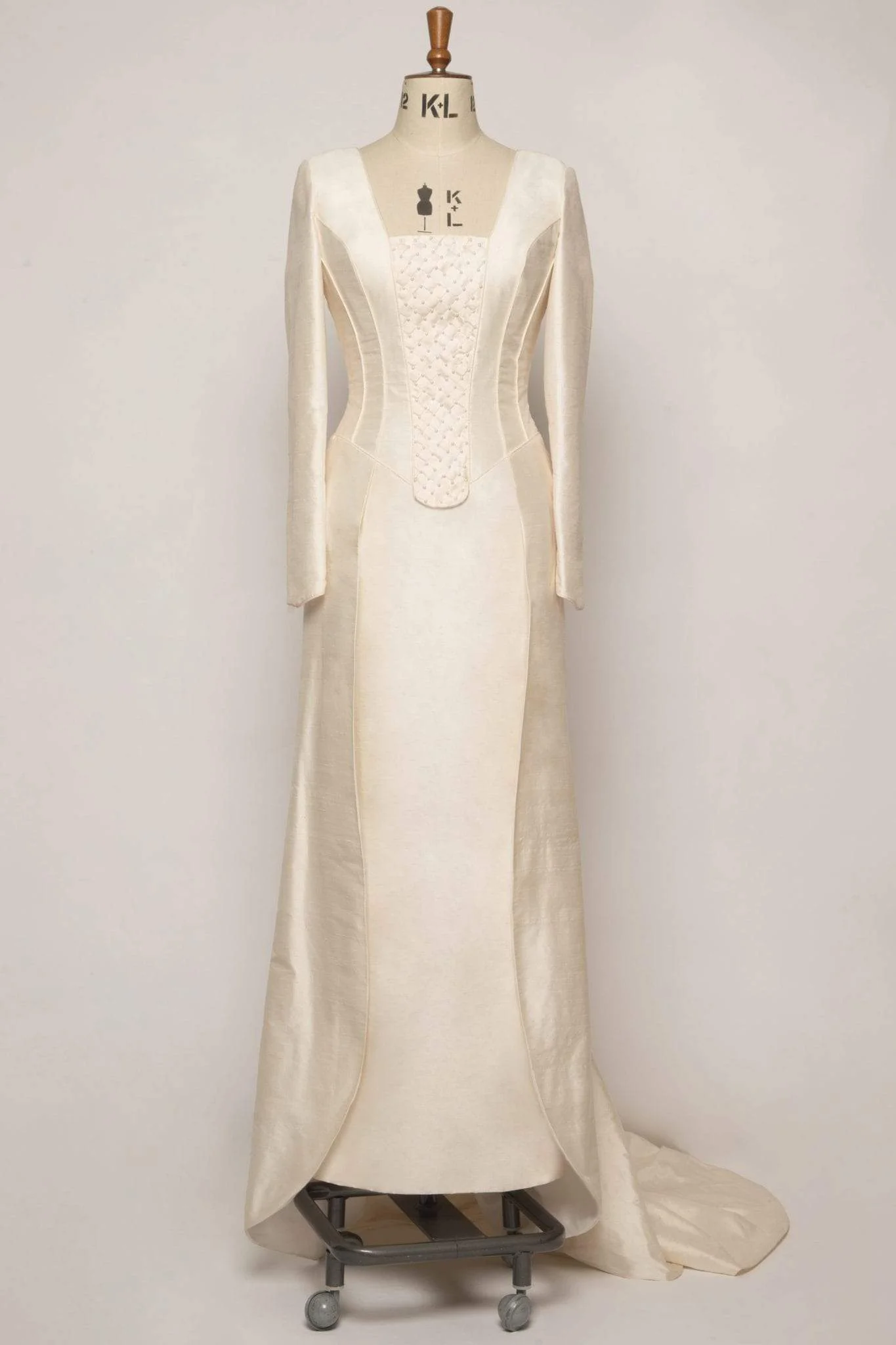 Exquisite long-sleeved silk dupion gown with square neckline, hand-sewn pearl detailing, piped edges, double pleated overskirt, and chapel train.