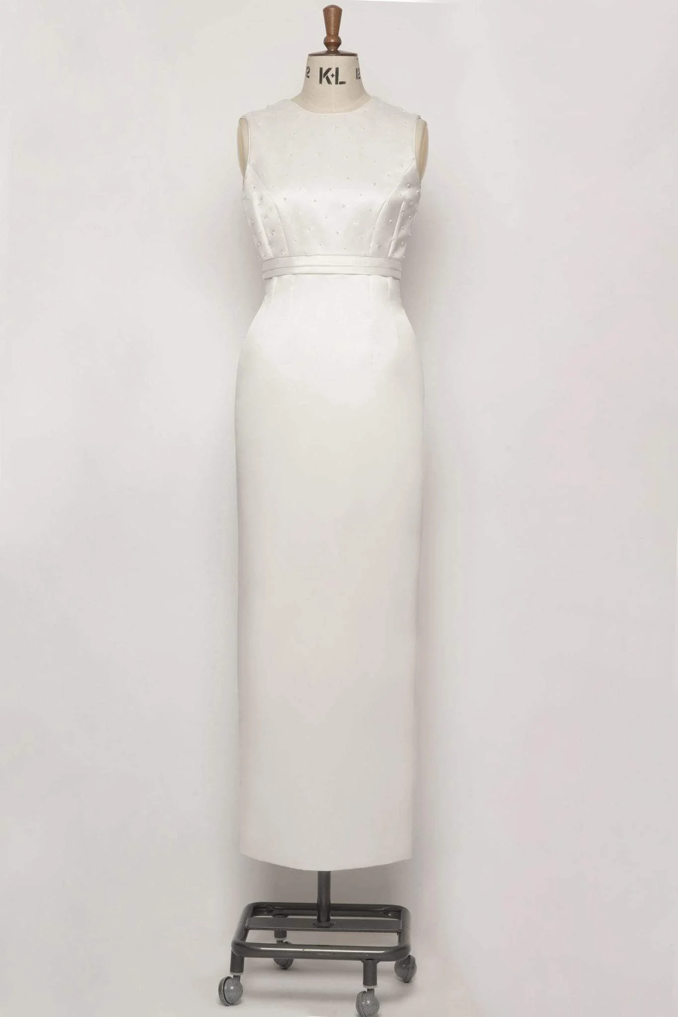 A stunning ivory duchess satin column dress with a high neck, low-cut square back, delicate beading, pleated bodice, and elegant piped edges.