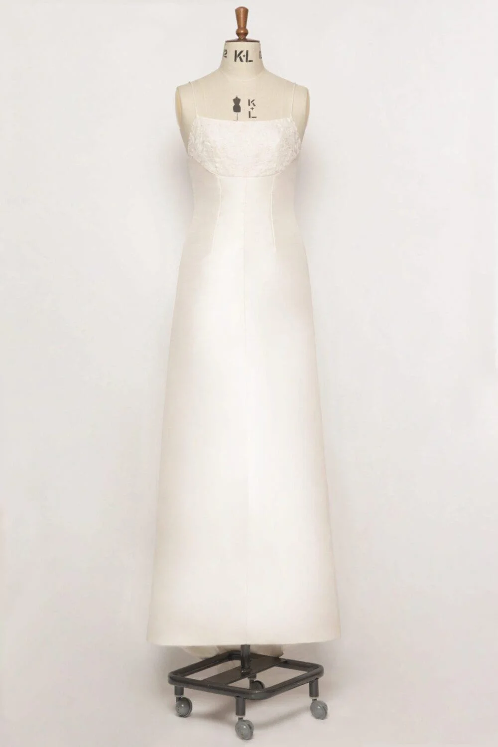 A-line silk dupion dress with a round neckline, spaghetti straps, embroidered bodice, covered working buttons at the back, and a mini puddle train.