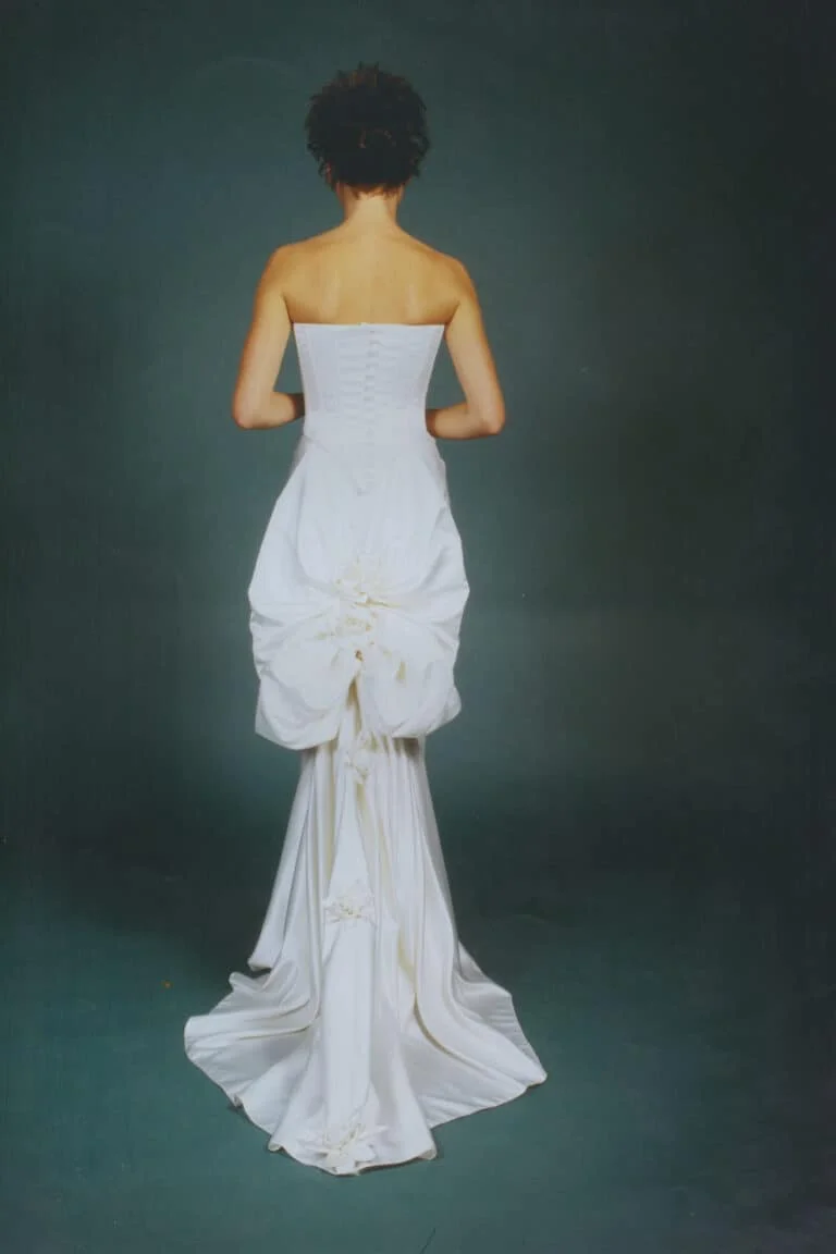 A structured bridal corset with smooth curves, soft drapes around the hips, and a dramatic skirt with hand-made flowers and bows in duchess satin.